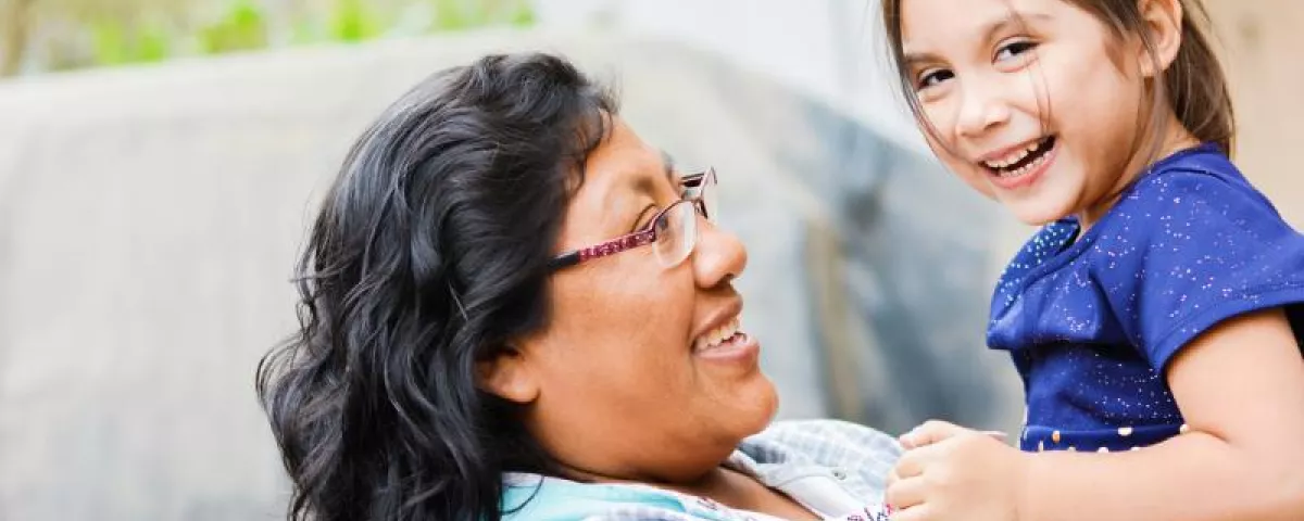 Mom hugging and carrying her daughter, both smiling. Tribal health partners.