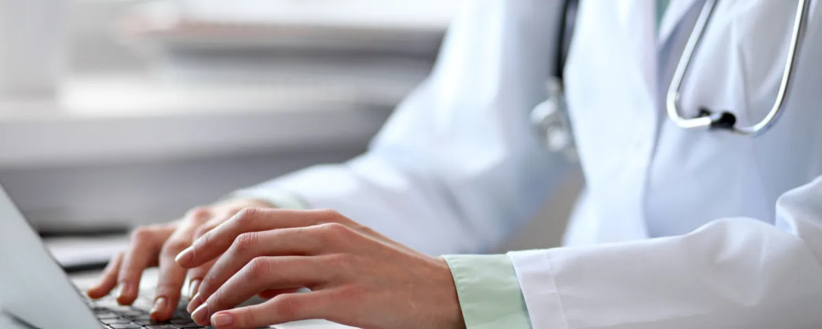 Hands of a doctor in lab coat typing into laptop computer