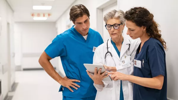 3 doctors in a hallway looking at a tablet