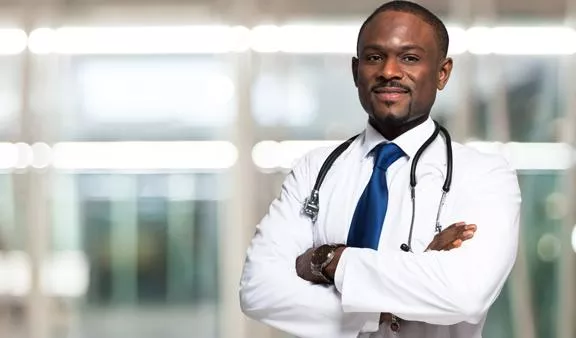 Medical billing services doctor in white shirt and blue tie wearing stethoscope around neck, crossing arms, and smiling at the camera.