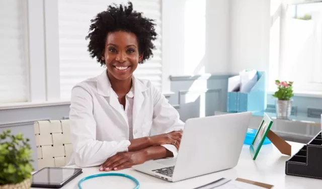 Doctor sitting in front of a computer, using practice management software and smiling into the camera.