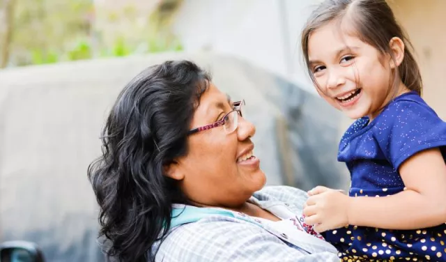 Mom hugging and carrying her daughter, both smiling. Tribal health partners.