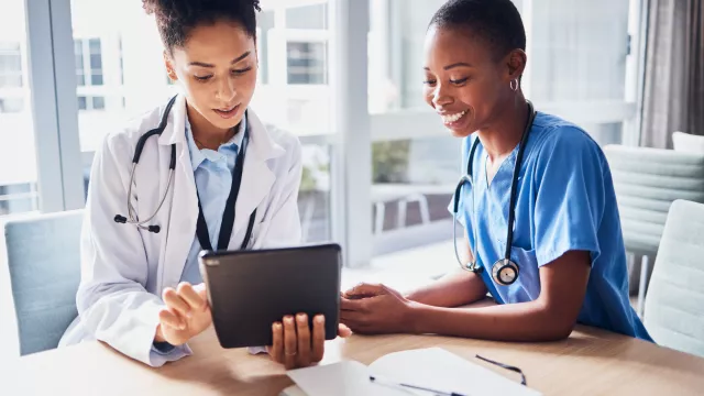 female doctor and female nurse looking at tablet and smiling