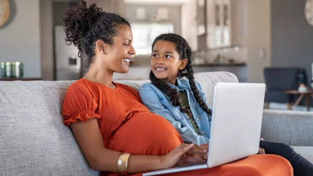 pregnant woman and daughter on couch with a computer on her lap