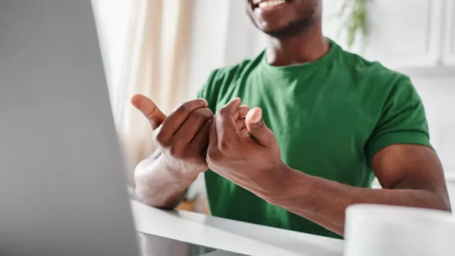 black man in green shirt using sign language in front of a computer