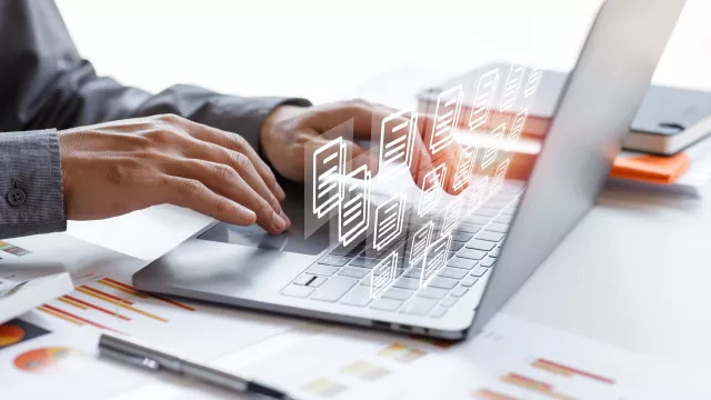 laptop on desk with hands typing and images of documents