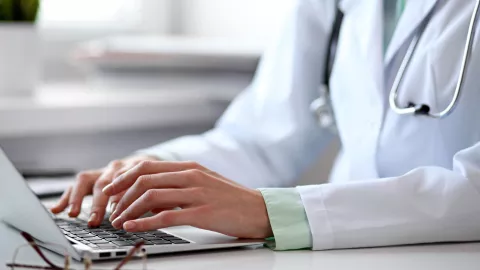 Hands of a doctor in lab coat typing into laptop computer